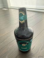 Closed bottle-shaped dispenser showing black body and teal label