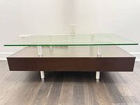 Front view showing tempered glass top, metal supports, dark brown base with drawers and metal feet