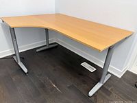 Perspective view of desk showing L-shape, light wood top, metal legs