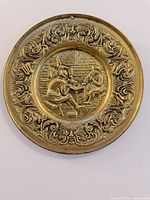 Round bronze wall plaque with ornate scroll border and two men in relief scene