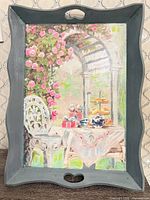 Front view of wooden tray showing painted floral garden patio scene and cut-out handles