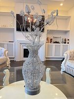 Full view of silver wire vase with decorative wire flowers on glass table