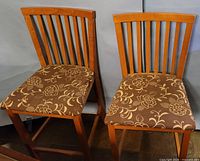 Front view of both counter-height chairs showing maple finish, slat backs, floral seat fabric