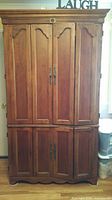 Closed view of full armoire showing paneled doors, crown top, scalloped base
