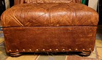 Front view of ottoman showing nailhead trim, leather wear, bun feet