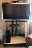 Front view of rolling TV stand with mounted TV, AV shelf, and wooden base platform
