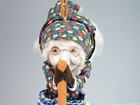 Front view of doll showing ceramic face, glasses, floral hood, holding spoon handle