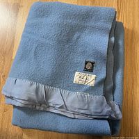 Folded blue wool blanket showing satin edge and attached labels