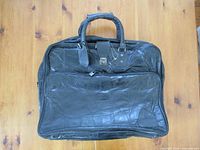 Front view showing leather patchwork exterior, top handles, lockable flap, large front pocket