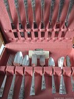 Flatware set arranged in pink-felt lined wooden chest showing pattern and quantity