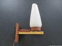 Side view of sconce showing brass arm, teak-look backplate, white glass shade