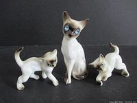 Front view of three porcelain Siamese cat figurines with blue rhinestone eyes