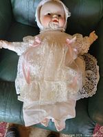 Full view of the doll lying on chair wearing lace gown and bonnet