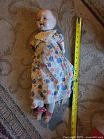 Full view of 20" composition doll with dress, tape measure beside for scale