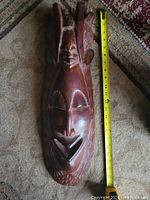 Front view of carved wooden tribal mask with measuring tape showing height