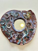 Front view showing entire round ceramic mirror with floral relief and central mirror glass