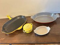All four Le Creuset pieces displayed: grill pan, large oval baking dish, mini cocotte, small ramekin