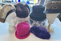 Group shot of all six hats on table and mannequins