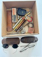Overview of all items inside cardboard box and two spectacle cases with sunglasses and eyeglass frame