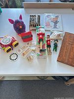 Group shot of all items including Furby, electronic clock toy, View-Master, reels, puppets, cribbage board, puzzle and small accessories