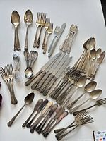 Full lot overview of mixed flatware laid out on white surface