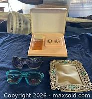 Fragrance set open with earrings, two sunglasses, ornate frame displayed
