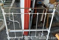 Full frontal view of white iron headboard with brass rail and finials