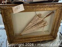 Full view of ornate gilt frame with folded lace parasol inside