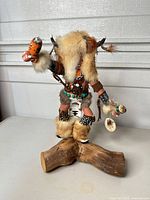 Front view of kachina doll on wood base showing overall appearance and accessories