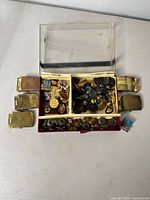 Open box showing assorted brass buttons, plastic buttons, insignia, and six belt buckles