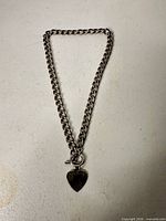 Full view of silver-tone curb-link necklace with heart pendant and toggle clasp