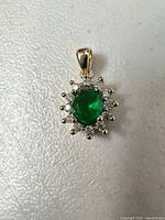 Front view of pendant showing oval green stone, clear halo stones, yellow gold-tone setting