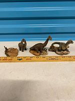 Group of three dinosaur figurines with detached leg piece shown beside ruler for scale