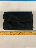 Front view of closed black leather clutch wallet with ruler for scale