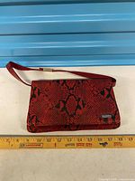 Full view of clutch purse with wrist strap and ruler for scale