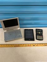 Group shot of Polaroid DVD player, Kobo eReader and DIGITZ calculator with ruler for scale