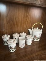 Full tea set displayed on shelf: teapot, five lidded cups, one open cup