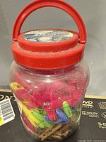 Full view of clear jar with red lid handle filled with clips and clothespins