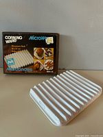 Boxed Corning Ware microwave rack beside loose rack