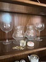Shelf with two stemmed goblets, two curved urn vases, small cube, round tin, metal script ornament