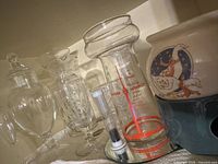 Group of clear glass containers and ceramic potpourri burner on shelf