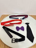 All five items laid out: three belts, bow tie, clip-on tie