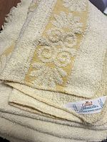 Stacked yellow terry towels showing floral scroll band and Cannon Monticello label