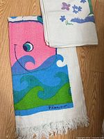 Whale towel and folded floral towel showing designs and signatures
