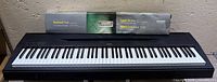Front view of Yamaha P-60 keyboard with boxed Casio stand on rear ledge