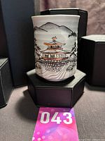 Front view of cylindrical earthenware vessel showing pagoda scene and scale reference