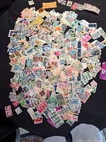 Wide view of entire pile of mixed loose stamps on dark surface