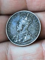 Obverse of the coin on fingertip showing King George V portrait