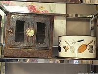Front view of rusted smoker/dehydrator box and white cake tin side by side on shelf
