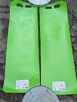two green plastic sleds side by side showing top surface, handles, and factory labels